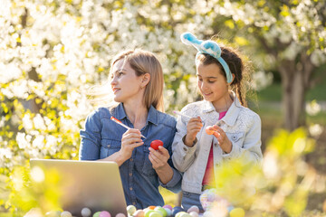 mother and daughter paint easter eggs with laptop, record lessons on a webcam with a laptop. mother...