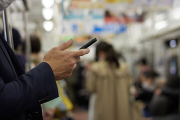 朝の通勤電車の中でスマートフォンを見ている中年サラリーマンの姿