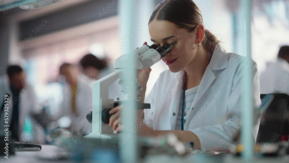 Poster portrait of young professional female engineer using a microscope in a lab to examine an electrical 