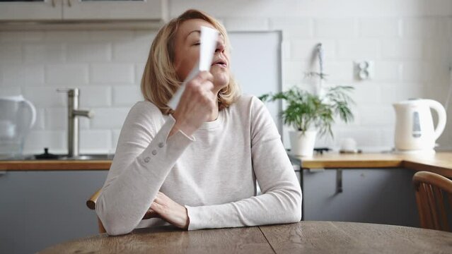 Mature woman sitting at home and having hot flush. Hormone imbalance, menopause concept 