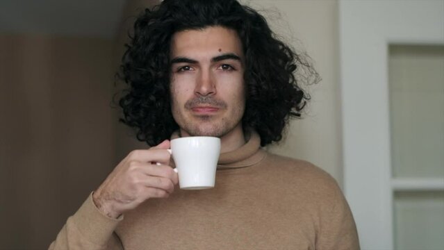 Slow Motion of a Sexy Caucasian Man Drinking Coffee and Looking to the Camera. Serious Look, Long Curly Hair.