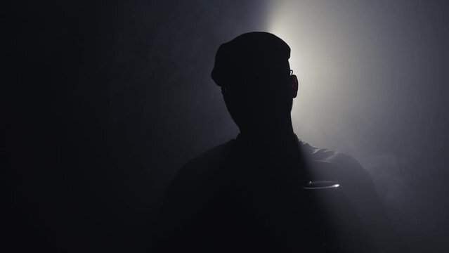 Mysterious businessman with hat holding a glass of drink backlit by cine background light and scene with smoke moving in slow motion
