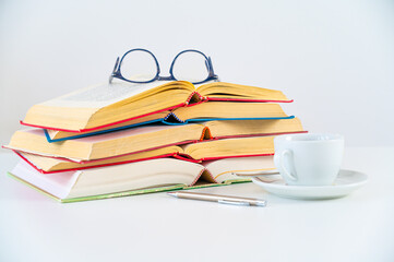 Stacks of books on a table, with a cup and glasses beside them. Study and culture.
