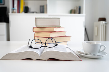 Stacks of books on a table, with a cup and glasses beside them. Study and culture.
