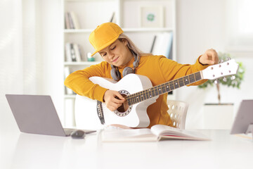 Young female tuning an acoustic guitar in front of a laptop computer
