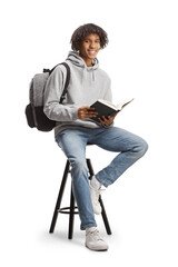 African american male student with a backpack sitting on a chair and holding an open book