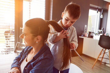 Son and mother play hairdresser combing hair at home