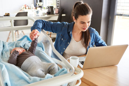 Mother works on the PC and takes care of her baby next to it
