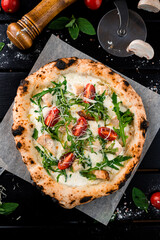 Pizza with cheese parmesan, chicken, arugula, cherry tomatoes and spices on a thick dough from oven.