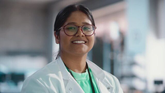 Portrait Close Up of Young Indian Female Specialist Wearing Lab Coat and Glasses Smiling. Professional and Successful Woman Working as an Engineer, Science Student in University Laboratory Posing