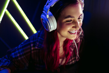 Smiling female gamer playing at night, wearing a headset in front of a computer