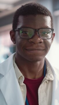 Vertical Screen: Portrait of Young Smiling Black Man Wearing Glasses and a Lab Coat Looking at the Camera. Future Engineer Pursuing Scientific Career. Manufacturing Student in University Posing