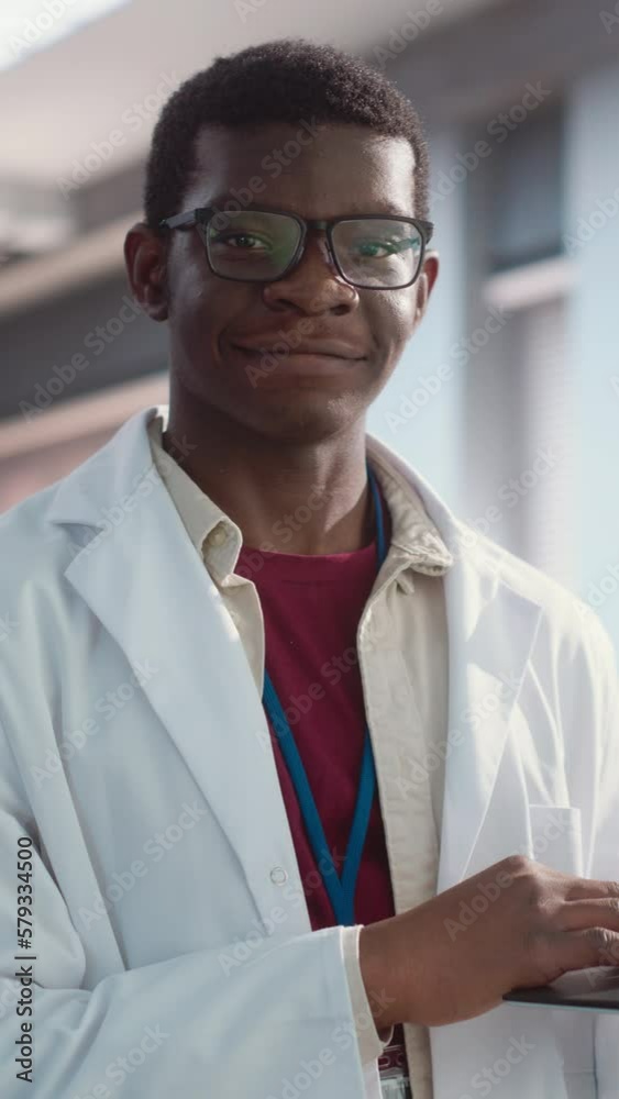 Poster vertical screen: portrait of black young male scientist using laptop computer, looking at camera and