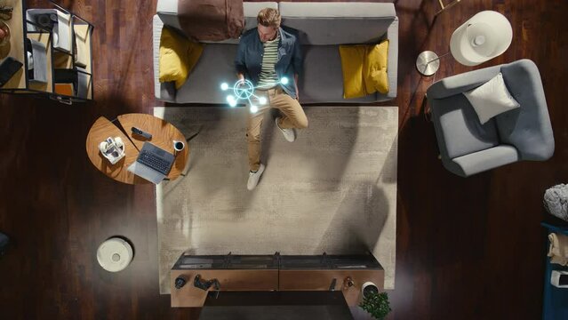 Top View Of Caucasian Man In the Loft Apartment Sitting Down on The Couch and Connecting Smartphone to Convenient Smart Home System. VFX Animation Visualizing Connected Devices. Laptop, TV, Speaker. - Powered by Adobe