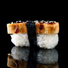Nigiri sushi with tamago omelet, rice, nori and unagi sauce on black.