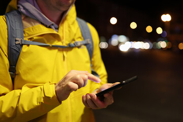 Male tourist in yellow coat using his smartphone outdoors.