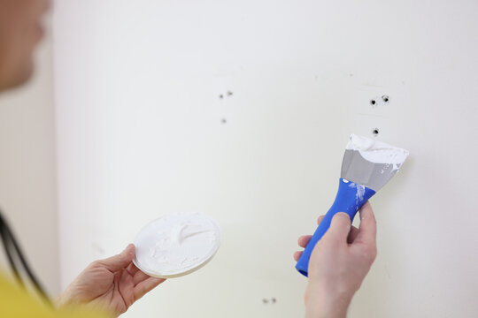 Worker or craftsman with putty knife plastering house wall.