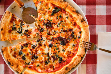 Italian pizza with dried tomatoes, sliced mozzarella cheese, lunch in a pizzeria. Top view with copy space for text. Cutlery on the table on the table.