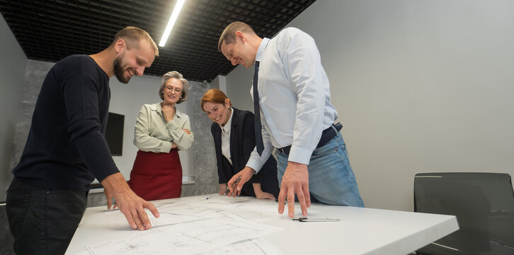Four business people review and discuss blueprints. Designers engineers at a meeting. 