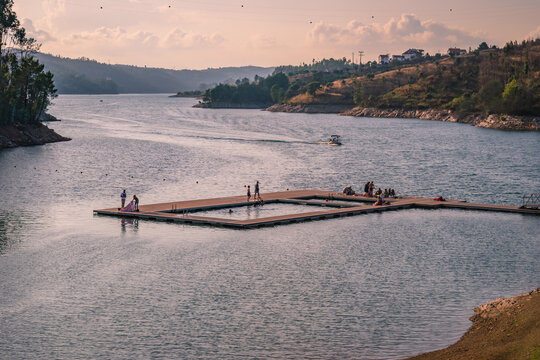 Platform on the river Z&ecirc;zere with silhouettes of vacationers and boat at sunset at Aldeia do Mato fluvial beach, Abrantes PORTUGAL