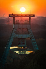 Vertical shot of a headframe tower with a golden sun setting in the background in Herten, Germany