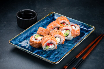 Sushi rolls with seared salmon, cream cheese, avocado, rice, nori, red flying fish caviar and soy sauce.