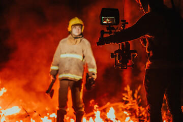 Fototapeta na wymiar A cameraman with professional equipment and stabilization for the camera recording the firefighter while performing work in a burning forest