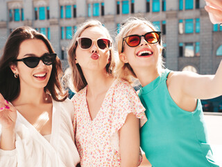 Three young beautiful smiling hipster female in trendy summer dresses  clothes. Sexy carefree women posing in the street. Positive models having fun, talking, chatting. Going crazy. Taking selfie