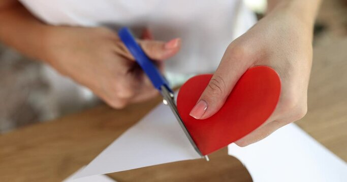 Woman hands cut out red heart from paper