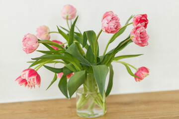 Stylish beautiful tulips bouquet in vase on wooden table in rustic room. Floral festive arrangement in farmhouse. Spring flowers composition. Happy mothers day and womens