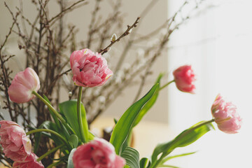 Stylish tulips and willow branches bouquet on wooden table close up. Floral festive arrangement in dining room in farmhouse. Spring flowers composition. Happy Easter!