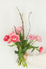 Stylish pink tulips with willow branches in hand on white wall background. Woman holding beautiful spring bouquet. Happy mothers day and womens day. Happy Easter