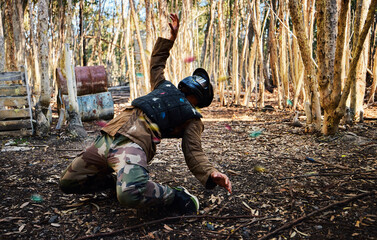 Man, paintball and dodging shots in the matrix for intense battle or war in the forest on knees. Male paintballer or soldier ducking to dodge paint balls in extreme adrenaline sports outdoors - obrazy, fototapety, plakaty