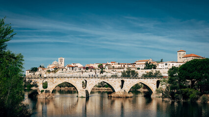 Fototapeta premium village with a roman bridge over a river on a clear day