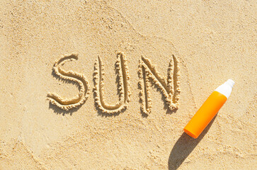 word Sun is written on sea sand. Orange bottle of sunscreen and word Sun on beach sand.