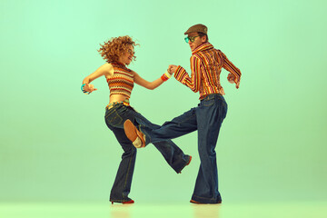 Two excited people, man and woman in retro style clothes dancing disco dance over green background. 1970s, 1980s fashion, music, hippie lifestyle,