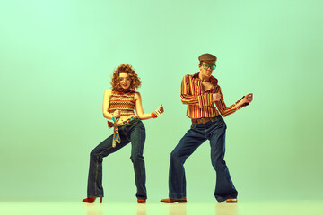 Feeling rhythm. Couple happy people, man and woman in retro style clothes dancing disco dance over green background. Concept of 1970s, 1980s fashion, hippie lifestyle