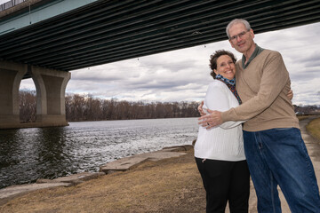 Older happy couple outside in late winter. High-quality photo showing a loving couple together outside near a river on a cloudy late winter day.