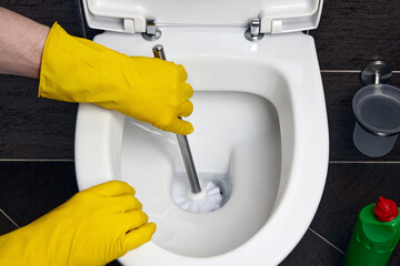 A man in yellow rubber gloves cleans the toilet with a brush and a disinfectant
