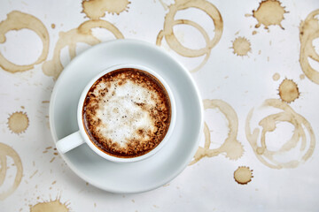A cup of tasty cappuccino coffee stands on a white background with coffee stains and splashes