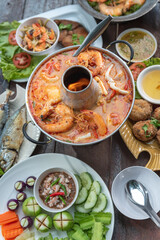 Tom Yam Kung or Tom Yum soup is Thai hot spicy soup shrimp or prawn with lemon grass, lemon, galangal, mushrooms, coconut milk and chili in bowl on wooden table top view, famous Thai food cuisine.