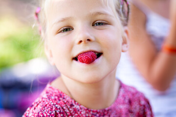 close-up child with raspberries in his mouth. Summer games with children. Healthy food. Summer vitamins. Family holiday