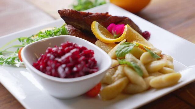 Duck fillet served on a white plater with a thin orange slice edible flower and potato dumplings. High quality 4k footage