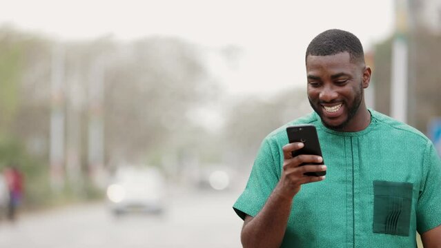 Young African Man holding smartphone outdoors, connects with friends on social media.