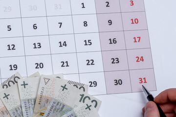 Kalendarz z długopisem trzymanym w dłoni wskazujący na ostatni - 31 dzień miesiąca 