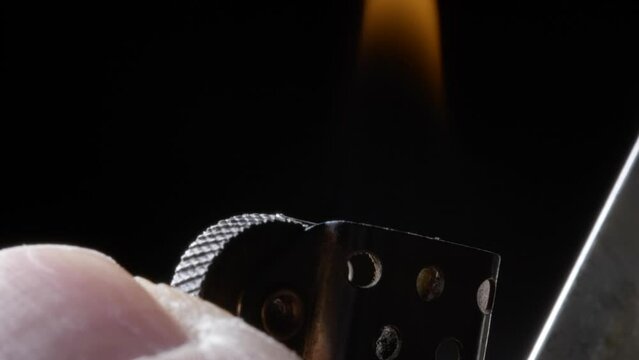 slow-motion close-up of a thumb striking a metal lighter igniting the blue flame