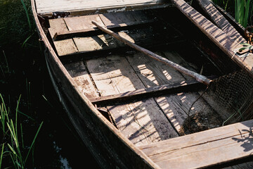 Fishing tackle inside of aged wooden boat moored on lake bank close up view. Rustic vessel for fishing industry.