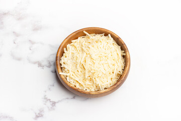 Queso rallado en hebras dentro de un cuenco de madera sobre un fondo blanco texturado de mármol. Vista superior y de cerca. Espacio de copia