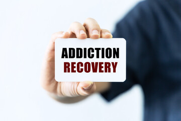 Addiction recovery text on blank business card being held by a woman's hand with blurred background. Business concept about addiction recovery.