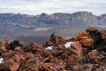 paisaje montañoso con mar de nubes, todo con tintes de color rojo y azul con algunas acumulaciones de nieve, vistas desde el teide